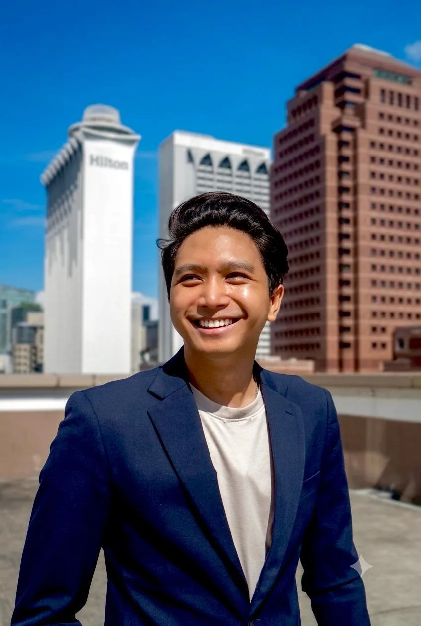 Kiangsak smiling in a navy blazer, with city towers behind him.