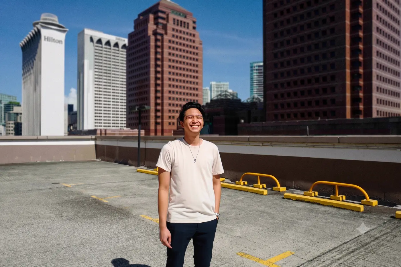 Kiangsak laughing on a rooftop car park, with hotel and office towers behind him.